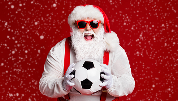 Weihnachtsmann h&auml;lt Fu&szlig;ball in den H&auml;nden und freut sich