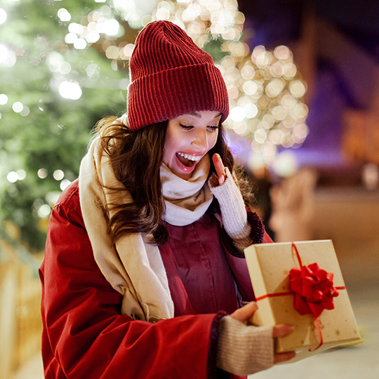 Frau schaut freudig in eine ge&ouml;ffnete Geschenkbox