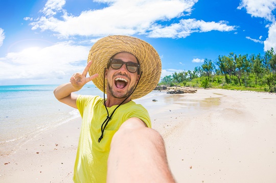 Selfie von einem jungen Mann am Strand mit Strohhut