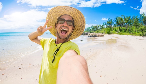 Selfie von einem jungen Mann am Strand mit Strohhut