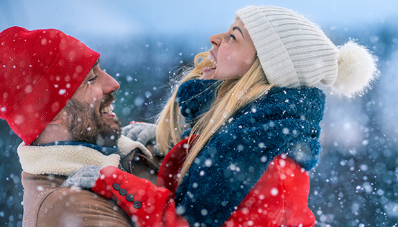 Junges Paar in Wintersachen umarmt und freut sich w&auml;hrend es schneit