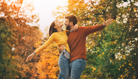 Junges Paar umarmt sich und freut sich in einem herbstlichen Park