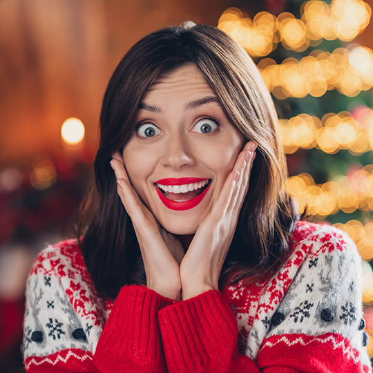 Frau im Weihnachtspullover freut sich erstaunt