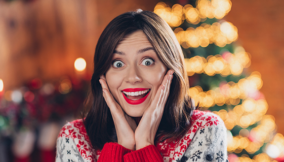 Frau im Weihnachtspullover freut sich erstaunt