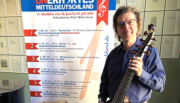 Gamben-Virtuose Thomas Fritzsch steht mit der Gambe vor dem Plakat Unerh&ouml;rtes MItteldeutschland 2026