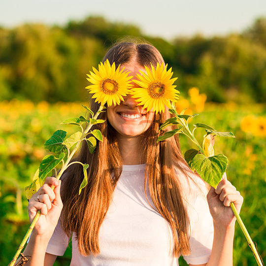 Fr&ouml;hliche junge Frau h&auml;lt Sonnenblumen vor den Augen