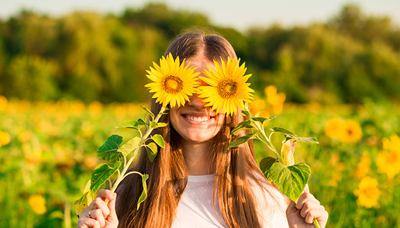 Junge Frau l&auml;chelnd mit Sonnenblumen vor den Augen