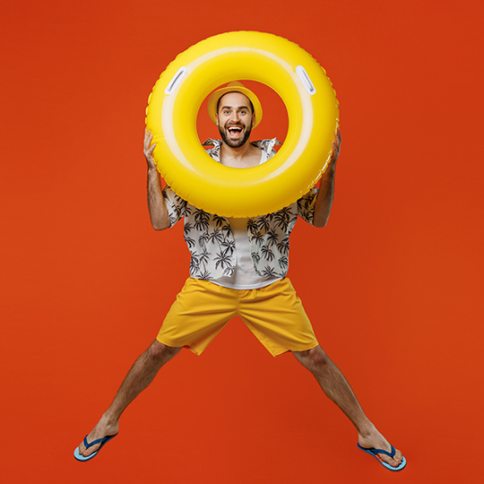 Mann in Sommerkleidung schaut erfreut durch einen gelben Schwimmreifen