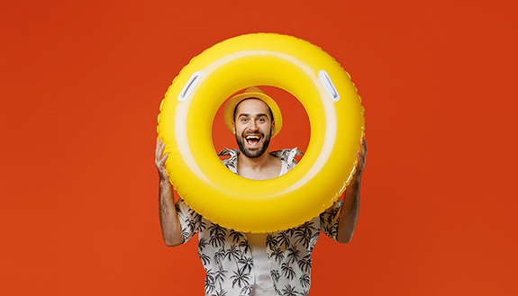 Mann in Sommerkleidung schaut erfreut durch einen gelben Schwimmreifen