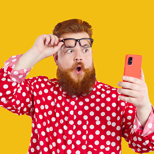 Ein Mann schaut erstaunt auf sein Handy und hebt dabei seine Brille auf die Stirn