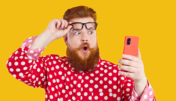 Ein Mann schaut erstaunt auf sein Handy und hebt dabei seine Brille auf die Stirn