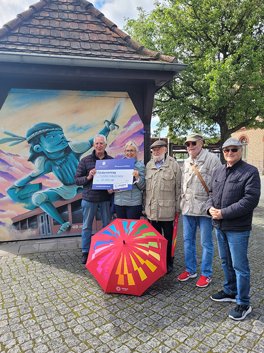 F&uuml;nf Personen mit symbolischen F&ouml;rderscheck vor Tunnelh&auml;uschen