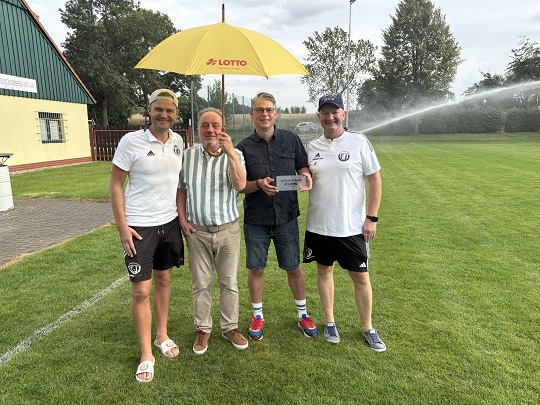 Jens u. Gero Stürzebecher, Rainer Jung, Andreas Lemke vom Ummendorfer Sportverein e. V. mit Regenschirm vor dem neuen Rasenbewässerungssystem