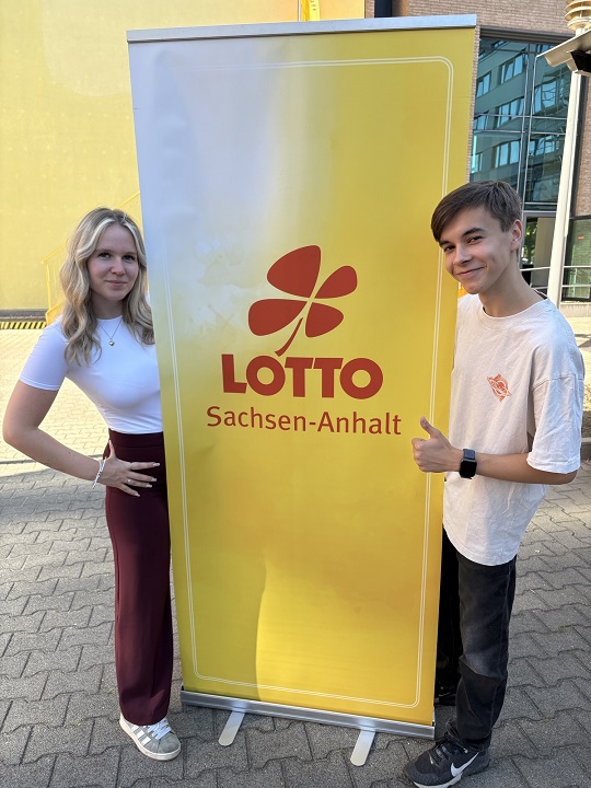 Azubis Lea Maria Luksche und Nils Leopold vor Banner von LOTTO Sachsen-Anhalt