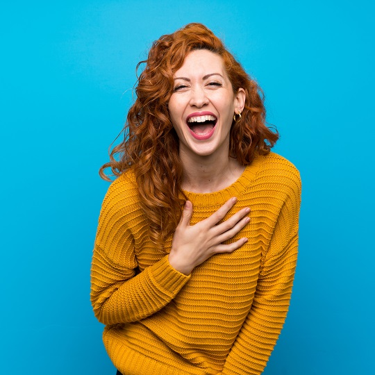 Rothaarige Frau mit gelbem Pullover lacht vor Freude