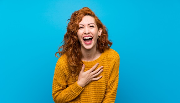 Rothaarige Frau mit gelbem Pullover lacht vor Freude