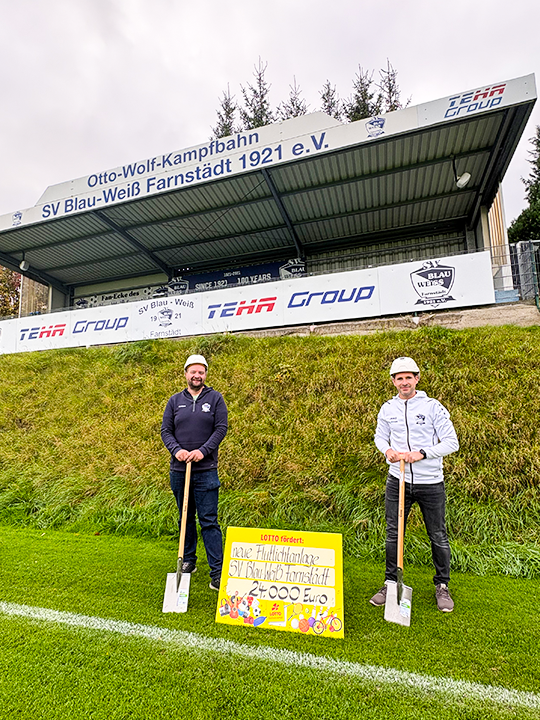 Zwei Personen mit LOTTO-F&ouml;rderscheck auf Sportplatz