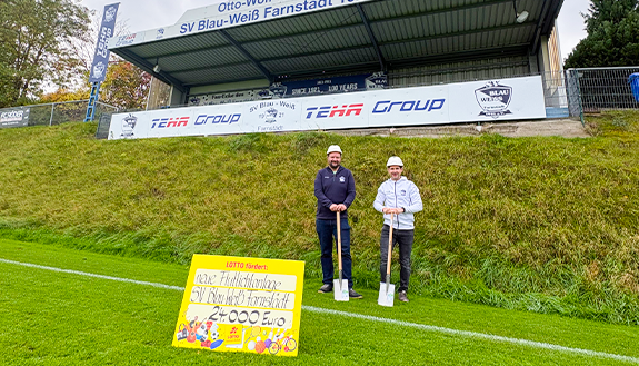 Zwei Personen mit LOTTO-F&ouml;rderscheck auf Sportplatz