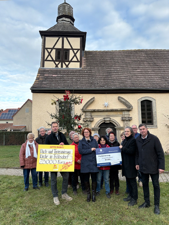 Mitarbeiter vor Kirche mit zwei symbolischen Scheck