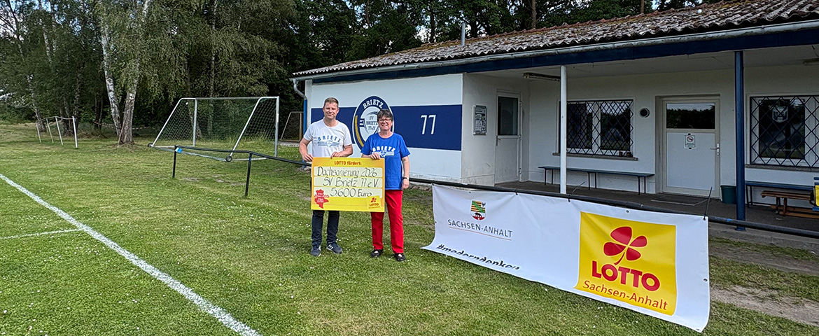 zwei Vereinsmitglieder mit symbolischen F&ouml;rderscheck vor Sportlerheim