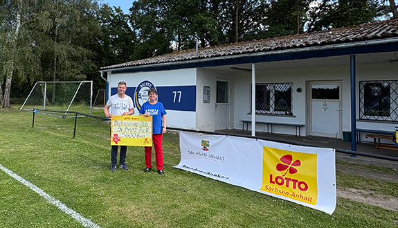 zwei Vereinsmitglieder mit symbolischen F&ouml;rderscheck vor Sportlerheim