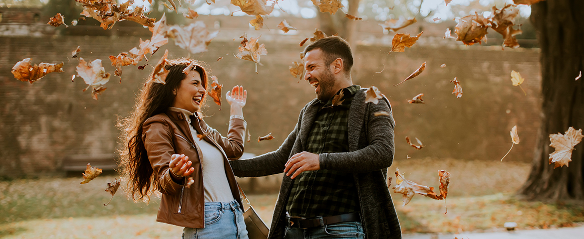 Junges Paar freut sich im fallenden Laub in einem herbstlichen Park