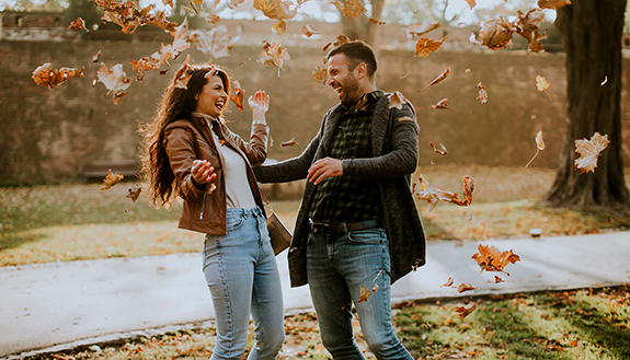 Junges Paar freut sich im fallenden Laub in einem herbstlichen Park