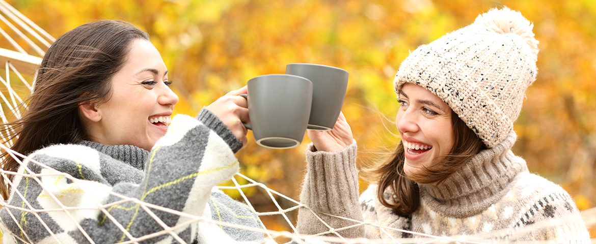 Zwei fröhliche Frauen stoßen mit Tassen im Herbst an