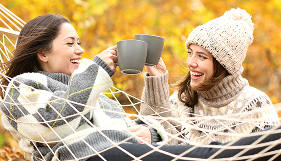 Zwei fröhliche Frauen stoßen mit Tassen im Herbst an